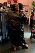 Load image into Gallery viewer, Full-body front view of a size 28 Eloquii black silky collared jumpsuit with a tie belt and pockets styled with colorful platform heels on a size 22/24 model.
