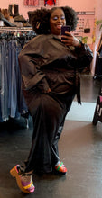 Load image into Gallery viewer, Additional full-body front view of a size 28 Eloquii black silky collared jumpsuit with a tie belt and pockets on a size 22/24 model, who is showing off the colorful platform shoes she&#39;s wearing.
