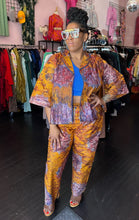 Load image into Gallery viewer, Full-body front view of a size 16 Le Victoria for RAYO orange, purple, blue, and maroon two-piece cotton button-up shirt and trouser set styled open over a cobalt blue crop top with heels and bejeweled glasses. The model stands in front of natural light and under overhead lights indoors.

