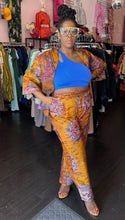 Load image into Gallery viewer, Additional full-body front view of a size 16 Le Victoria for RAYO orange, purple, blue, and maroon two-piece cotton button-up shirt and trouser set styled open over a cobalt blue crop top with heels and bejeweled glasses. The model stands in front of natural light and under overhead lights indoors.
