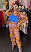 Load image into Gallery viewer, Final full-body front view of a size 16 Le Victoria for RAYO orange, purple, blue, and maroon two-piece cotton button-up shirt and trouser set styled open over a cobalt blue crop top with heels and bejeweled glasses. The model stands in front of natural light and under overhead lights indoors.
