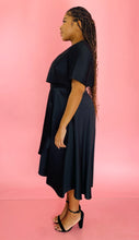 Load image into Gallery viewer, Full-body side view of a size 14 Jason Wu for 11HONORÉ black a-line midi dress with a subtle high-low draping styled with black heels on a size 14 model.
