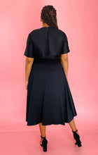Load image into Gallery viewer, Full-body back view of a size 14 Jason Wu for 11HONORÉ black a-line midi dress with a subtle high-low draping styled with black heels on a size 14 model.
