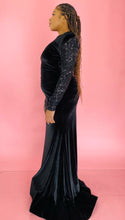 Load image into Gallery viewer, Full-body side view of a size 12/14 Melissa Mercedes black velvet floor-length gown with a high neckline, shoulder pad detail, black mesh and sequin sleeves and back, and a train on a size 14 model.

