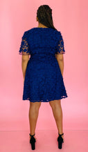 Load image into Gallery viewer, Full-body back view of a size 14 Adrianna Papell navy blue midi dress with floral appliques and sheer mesh sleeves styled with black strappy heels on a size 14 model.
