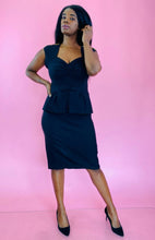 Load image into Gallery viewer, Additional full-body front view of a size 18 Stop Staring black peplum midi dress with square-sweetheart neckline, ruching at the bust, and a bow detail at the waist styled with black pumps on a size 10/12 model.
