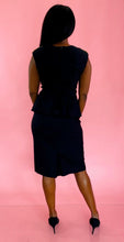 Load image into Gallery viewer, Full-body back view of a size 18 Stop Staring black peplum midi dress with square-sweetheart neckline, ruching at the bust, and a bow detail at the waist styled with black pumps on a size 10/12 model.
