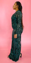Load image into Gallery viewer, Full-body side view of a size 12/14 Melissa Mercedes emerald green body-hugging floor-length gown with intricate mesh, bead, and sequin work all throughout and a slit at the back on a size 14 model.
