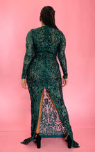 Load image into Gallery viewer, Full-body back view showing off the high, back slit of a size 12/14 Melissa Mercedes emerald green body-hugging floor-length gown with intricate mesh, bead, and sequin work all throughout and a slit at the back on a size 14 model.
