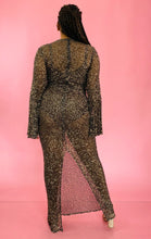 Load image into Gallery viewer, Full-body back view showing off the back slit of a size 12/14 Melissa Mercedes sheer brown floor-length gown with gold sequin all-over pattern, wide bell sleeves, and back slit on a size 14 model.
