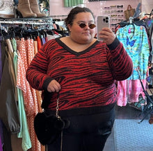 Load image into Gallery viewer, Closer front view of a size 20/22 Brave Soul red and black tiger striped sweater with black trim collar and cuffs styled with black pants and a black fluffy bag on a size 24/26 model.
