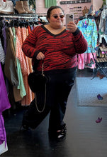 Load image into Gallery viewer, Full-body front view of a size 20/22 Brave Soul red and black tiger striped sweater with black trim collar and cuffs styled with black pants and a black fluffy bag on a size 24/26 model.
