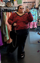 Load image into Gallery viewer, Additional full-body front view of a size 20/22 Brave Soul red and black tiger striped sweater with black trim collar and cuffs styled with black pants and a black fluffy bag on a size 24/26 model.
