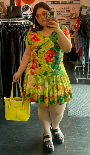 Full-body front view of a size 2X Jams World vintage chartreuse yellow hawaiian floral mini dress with pink, yellow, and green floral and tiered skirt styled with a yellow purse and black slides on a size 14/16 model.