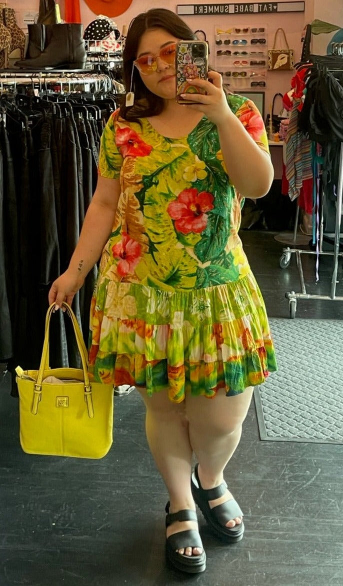 Full-body front view of a size 2X Jams World vintage chartreuse yellow hawaiian floral mini dress with pink, yellow, and green floral and tiered skirt styled with a yellow purse and black slides on a size 14/16 model.