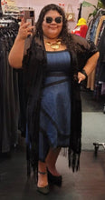 Load image into Gallery viewer, Full-body front view of a size 24 Eloquii medium-dark wash denim midi dress with an asymmetrical hem and black piping details styled with black lace duster, black flats, and chunky jewelry on a size 24 model.
