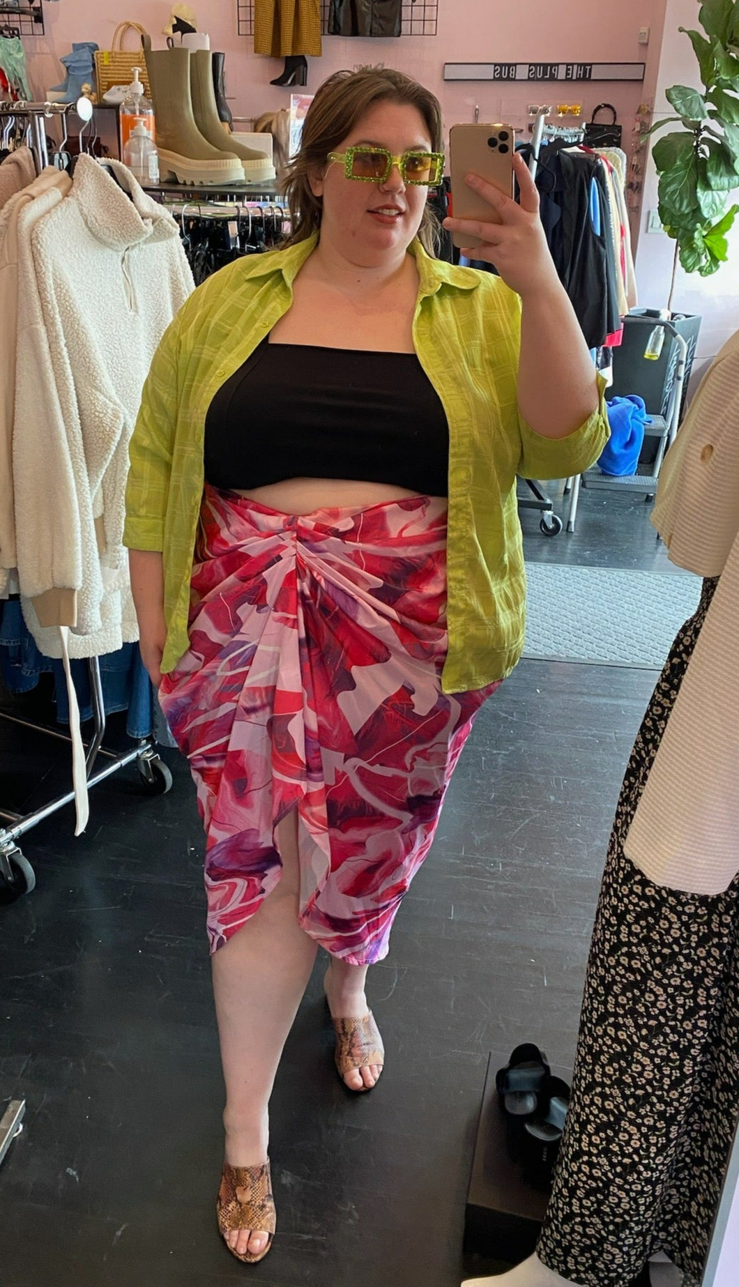 Front view of a size 24 Pretty Little Thing hot pink, light pink, purple, and white abstract watercolor patterned gathered midi skirt styled with a black tank and acid green button-up top on a size 24 model.