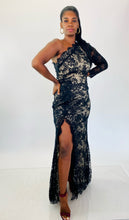Load image into Gallery viewer, Full-body front view of this size 16 Monique Lhuillier for 11Honoré one-shoulder cream gown with sheer black lace overlay and high side slit styled with maroon strappy heels on a size 12 model.
