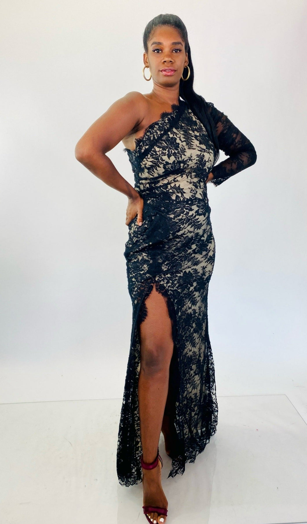 Full-body front view of this size 16 Monique Lhuillier for 11Honoré one-shoulder cream gown with sheer black lace overlay and high side slit styled with maroon strappy heels on a size 12 model.