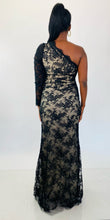 Load image into Gallery viewer, Full-body back view of this size 16 Monique Lhuillier for 11Honoré one-shoulder cream gown with sheer black lace overlay and high side slit styled with maroon strappy heels on a size 12 model.
