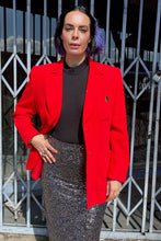 Load image into Gallery viewer, Additional front view of a size 14 (fits like 12) Yves Saint Laurent vintage red blazer with large gold buttons and pocket details styled over a black blouse and silver sequin pencil skirt on a size 10 model. The photo is taken outside in natural lighting.
