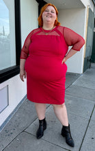 Load image into Gallery viewer, Full-body front view of a size 24 Lane Bryant red sheath midi dress with a faux-halter style neckline and long sheer mesh swiss dot sleeves styled with gold jewelry and black boots on a size 22/24 model.
