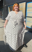 Load image into Gallery viewer, Additional full-body front view of a size 4X Rebdolls white and black polka dot ruffle-tiered maxi dress with ruffle sleeves and tie belt styled with leather boots and a leather hat on a size 22/24 model. Photo is taken outside in the sun.
