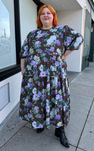 Load image into Gallery viewer, Additional full-body front view of a size 26 ASOS dark olive green, vibrant green, and lavender mixed print floral and plaid tiered maxi dress with puff sleeves styled with black boots on a size 22/24 model. The photo is taken outside in natural lighting.
