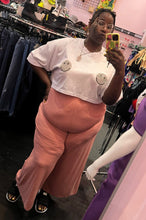 Load image into Gallery viewer, Full-body front view of a pair of size 3X Zelie for She dusty pink stretch high-waisted pants styled with a white smiley face tee and black slides on a size 24/26 model.
