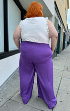Load image into Gallery viewer, Full-body back view of a pair of size 28 Eloquii purple lightweight wide leg pants with elastic waistband styled with a white ruffled tank and black boots on a size 22/24 model.

