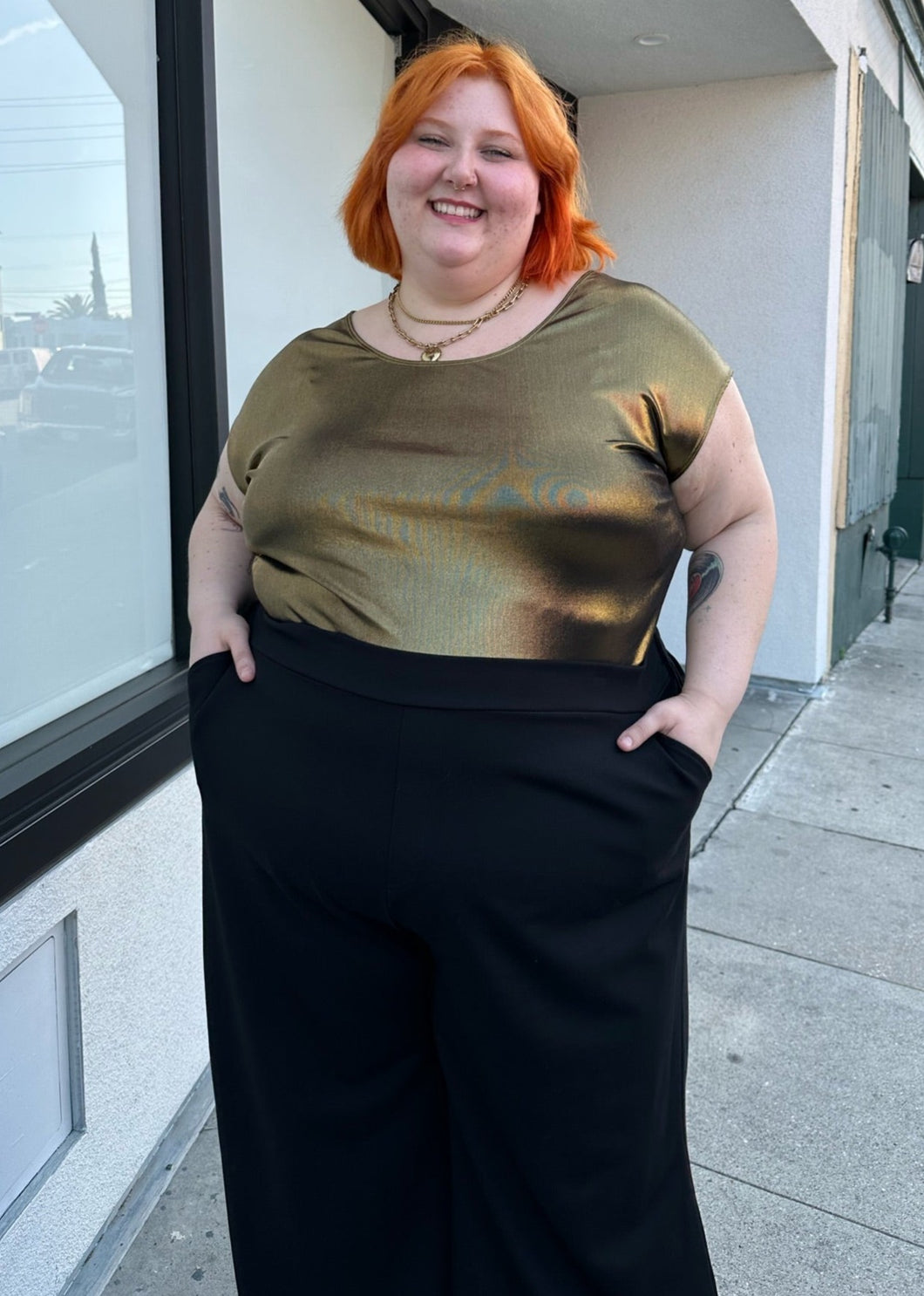 Front view of a size S (fits like 2/3X) American Apparel vintage metallic gold backless scoop neck top styled tucked into black wide leg pants on a size 22/24 model.