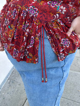 Load image into Gallery viewer, Close up view of the cute side slits on a size 1/2X deep red, white, teal, yellow, and purple multicolor floral baby doll blouse with long sleeves, a drawstring neckline, and side slits on a size 22/24 model.
