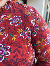 Load image into Gallery viewer, Close up view of the mixed floral pattern and gathered neckline on a size 1/2X deep red, white, teal, yellow, and purple multicolor floral baby doll blouse with long sleeves, a drawstring neckline, and side slits on a size 22/24 model.
