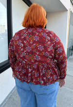 Load image into Gallery viewer, Back view of a size 1/2X deep red, white, teal, yellow, and purple multicolor floral baby doll blouse with long sleeves, a drawstring neckline, and side slits styled with light wash denim on a size 22/24 model.
