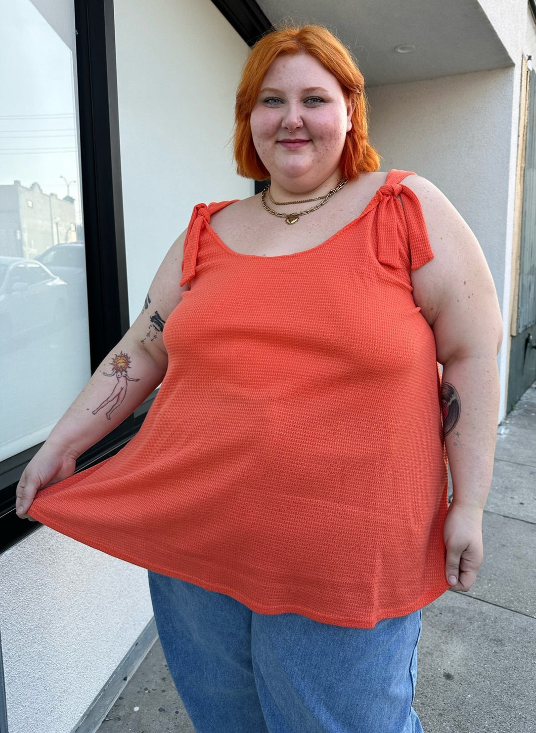 Front view of a size 26/28 Limited Collection neon coral tie-strap textured tank top styled over light wash jeans on a size 22/24 model.