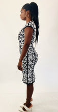 Load image into Gallery viewer, Full-body side view of this size M Michael Kors black and white textured floral sheath midi dress with cap sleeves styled with strappy white heels on a size 12 model.
