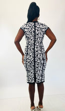 Load image into Gallery viewer, Full-body back view of this size M Michael Kors black and white textured floral sheath midi dress with cap sleeves styled with strappy white heels on a size 12 model.
