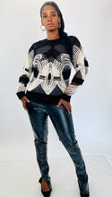 Load image into Gallery viewer, Full-body front view of a size XL Naeem Khan black and white velvet, mesh, and beaded long sleeve blouse styled with black pleather pants and black pumps on a size 12 model.
