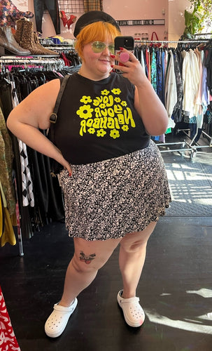 Full-body front view of a size 3X Forever 21 black and white ditsy floral mini circle skirt styled with a black tank and white crocs on a size 22/24 model.
