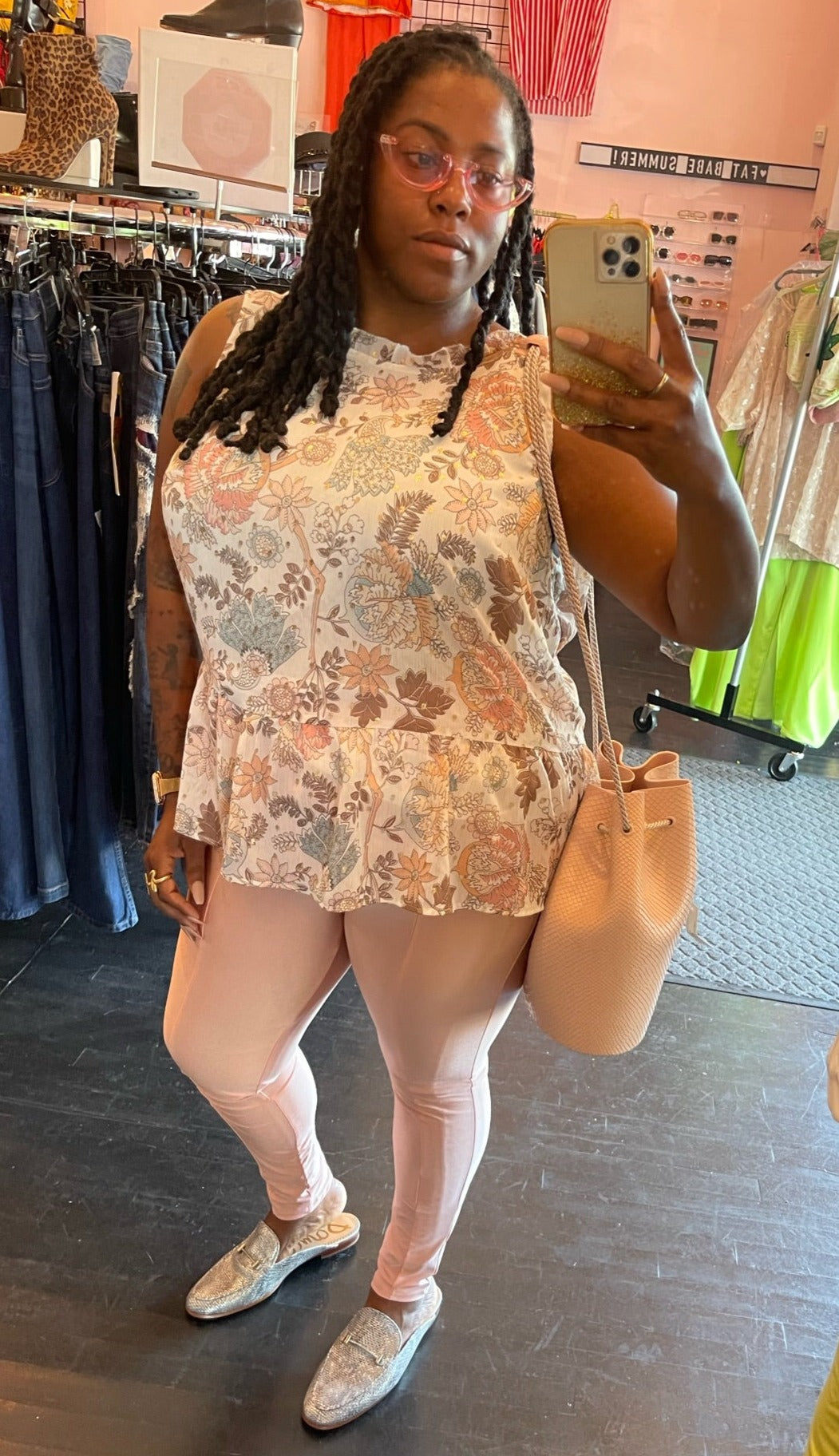 Full-body front view of a size 20 Loft white, pink, peach, and light blue mixed floral pattern sheer-leaning tank blouse with gold foiling and a ruffle hem styled with light pink skinny jeans and silver slides on a size 16/18 model.