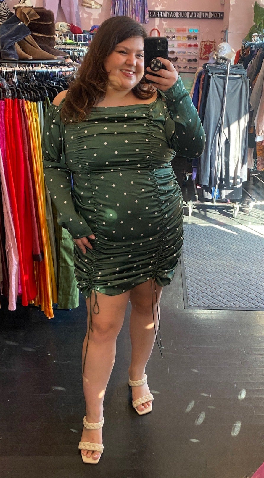 Full-body front view of a size 1X Fashion Nova emerald green and white mini polka dot ruched mini dress with long sleeves, a square neckline, and drawstring adjustable length styled with tan braided heels on a size 14/16 model.