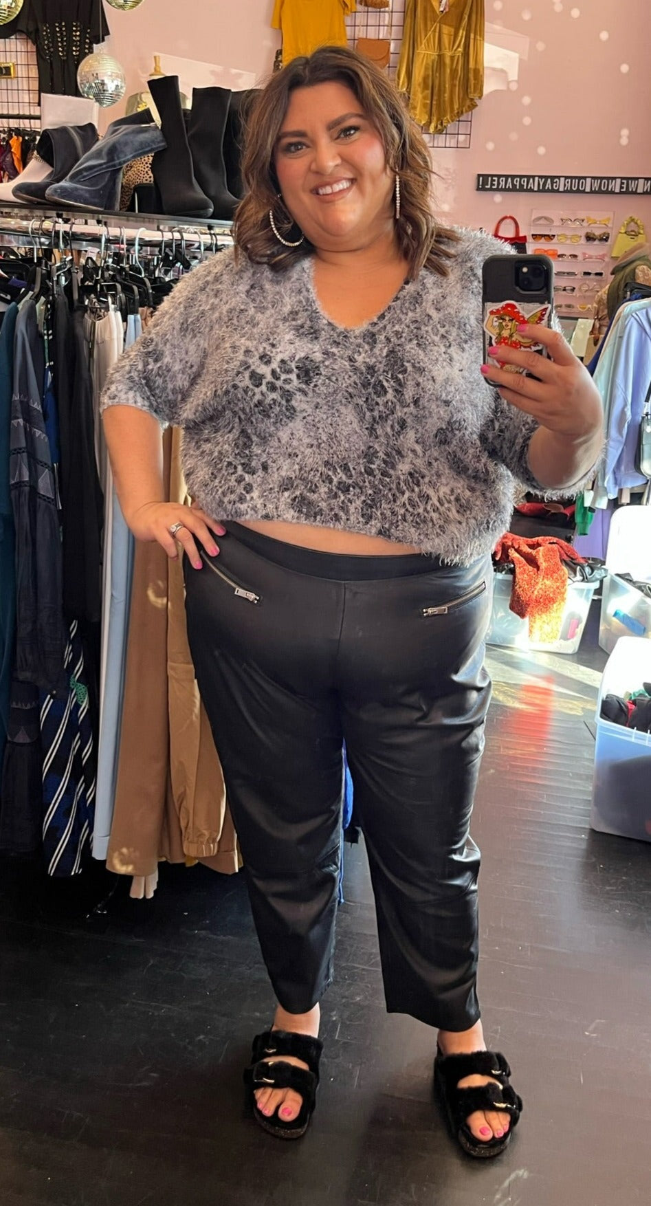 Full-body front view of a pair of size 26 Ellos black genuine leather tapered pants with zipper pockets styled with a gray fuzzy cropped sweater and black slides on a size 18/20 model.