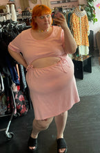 Load image into Gallery viewer, Additional full-body front view of a size 4 Fashion to Figure baby pink short sleeve sweatshirt-style midi dress with a drawstring belly cut-out styled with a floral choker and black slides on a size 22/24 model.
