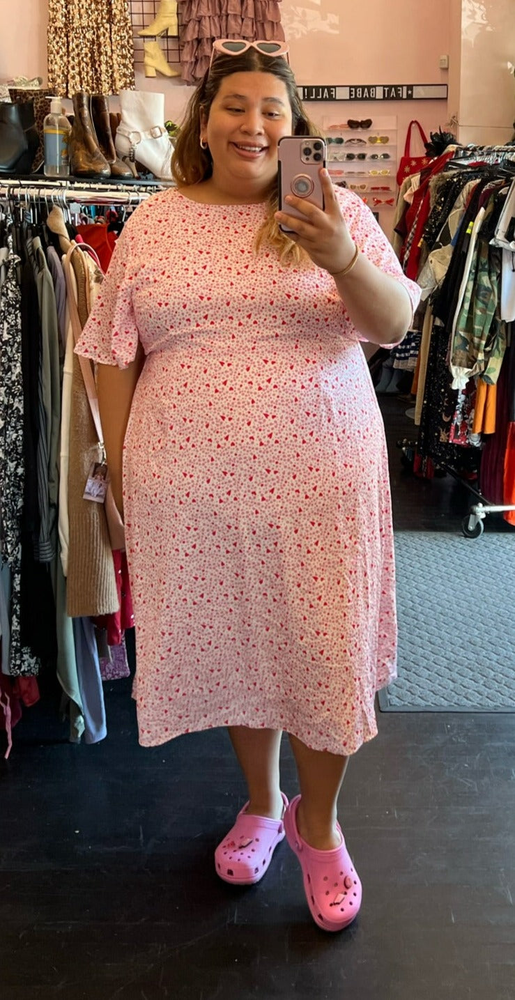 Full-body front view of a size 22 Glamorous Curve white midi dress with baby pink and red polka dot and heart mixed print styled with pink crocs on a size 20/22 model.