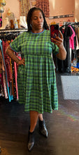 Load image into Gallery viewer, Full-body front view of a size XXL Rudie vibrant green plaid babydoll style midi dress styled with black boots on a size 16 model.
