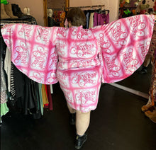Load image into Gallery viewer, Full-body back view showing off the length and span of the bell sleeves of a size 4XL Fashion Brand Company pink month mini dress with &quot;Jewish Girls&quot; cursive all-over pattern styled with black combat boots on a size 24 model. The photo is taken inside in front of a window, combining natural light and overhead lighting.
