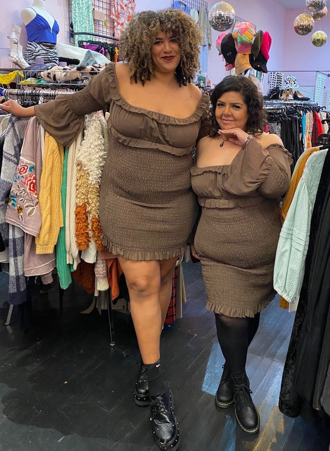 Full-body front view of a size 18 and a size 16 Pretty Little Thing neutral tone brown smocked-body off-shoulder-optional mini-midi dress with ruffle details and a bell sleeves styled with black shoes on a size 16/18 and 14/16 model, respectively.