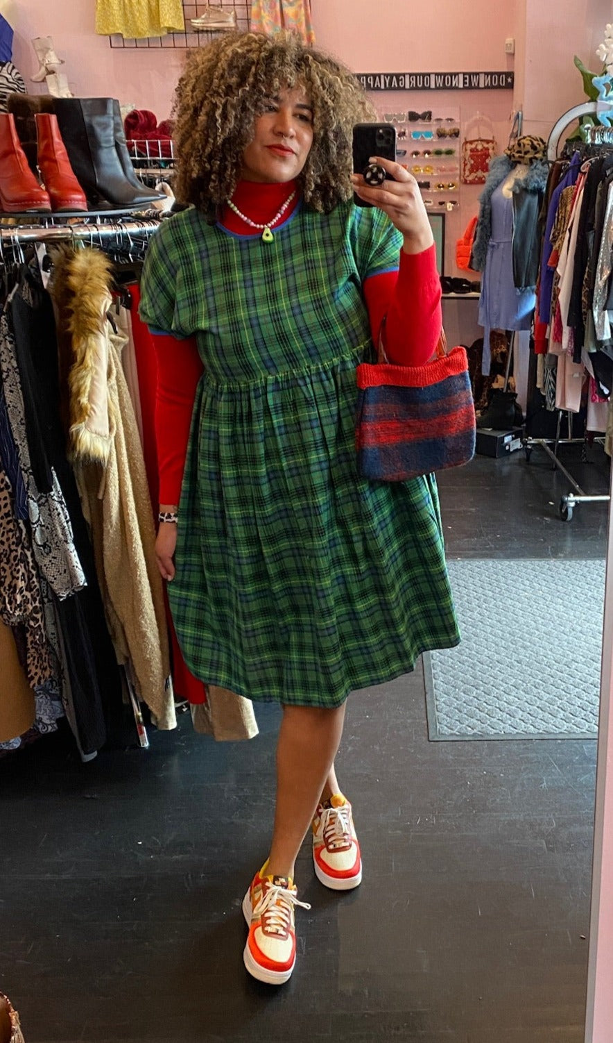 Full-body front view of a size XXL Rudie vibrant green plaid babydoll style midi dress styled over a red turtleneck with red and white sneakers on a size 16/18 model.