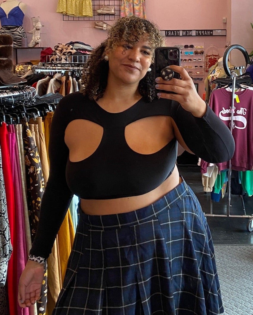 Front view of a size 12 Pretty Little Thing black long sleeve crop top with décolletage cut out details styled with a blue and black plaid mini skirt on a size 16/18 model.