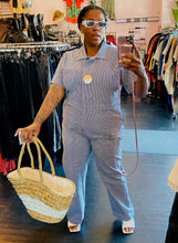 Load image into Gallery viewer, Additional full-body front view of a size XXXL Nooworks blue and white pinstriped jumpsuit with collar and breast pocket styled with blue sunglasses and an oversize wicker bag on a size 16 model.
